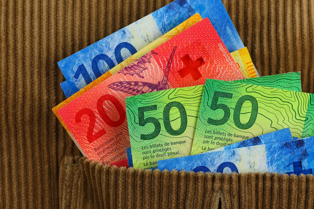 Billets en francs suisses dépassant d’une poche de pantalon, symbolisant le salaire d’un frontalier suisse.