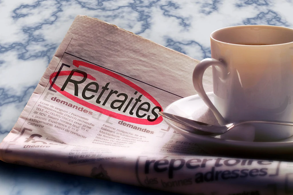 Journal ouvert avec le mot « Retraites » entouré en rouge et tasse de café sur table en marbre, symbolisant la déclaration retraite suisse en France
